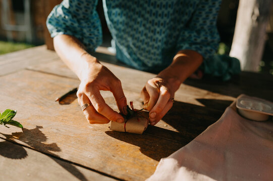 Hands tying twine around small wrapped parcel on wooden table during handmade eco packaging work outdoors