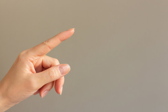 Close-up photo of a woman's index finger pointing at an empty beige background, ordering something on a virtual screen.
