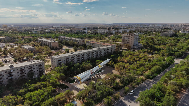 Aerial view of the Baikonur Cosmodrome rocket monument situated among residential apartment buildings and lush green trees in Karmakshy District, Kyzylorda Region, Kazakhstan.