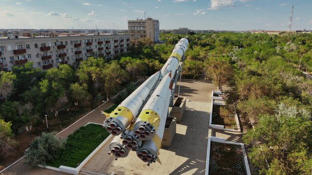 Aerial view of the Soyuz rocket monument at Baikonur Cosmodrome, surrounded by lush green trees and residential buildings in Karmakshy District, Kyzylorda Region, Kazakhstan.