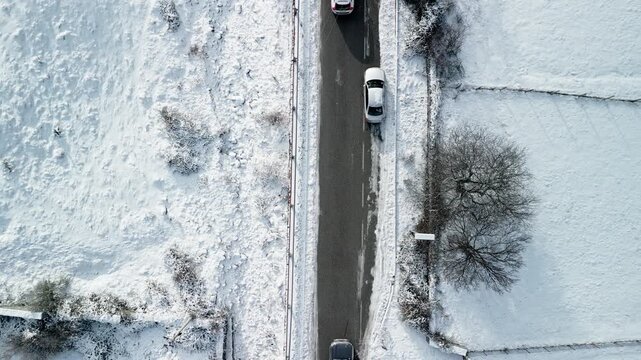 Albania, Boge 11 01 2026: Top-down still 4K drone video of cars and pickup truck driving and parking along dark asphalt road in Boge, flanked by snowy terrain and frozen riverbed.