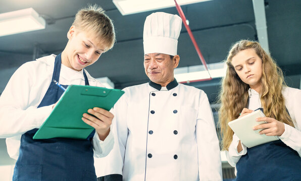 Senior male chef teaches young teenage boys cooking in school kitchen. Education Concept