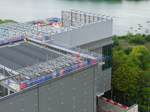 Aerial view of a data center under construction with scaffolding and metal framework on the roof, situated near a body of water in the United Kingdom.