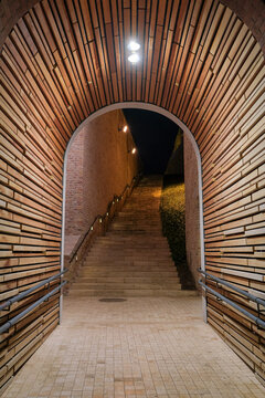 Night view of an illuminated arched pedestrian passage with wooden wall cladding and stone stairs near the Buda Castle Tunnel on Castle Hill in Budapest, Hungary.