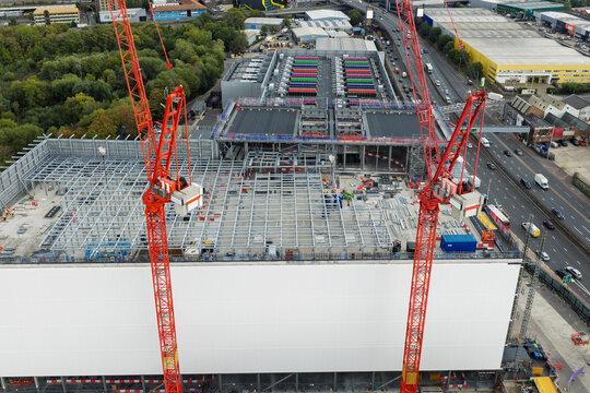 Aerial view of a data center construction site featuring two prominent red tower cranes, steel framework, and industrial surroundings in the United Kingdom.