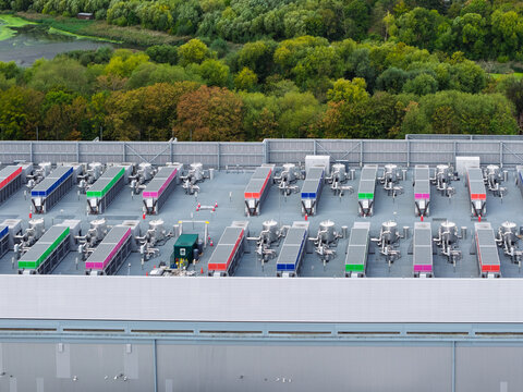 Aerial view of a data center roof featuring rows of colorful cooling units and ventilation systems set against a backdrop of lush green trees in the United Kingdom.