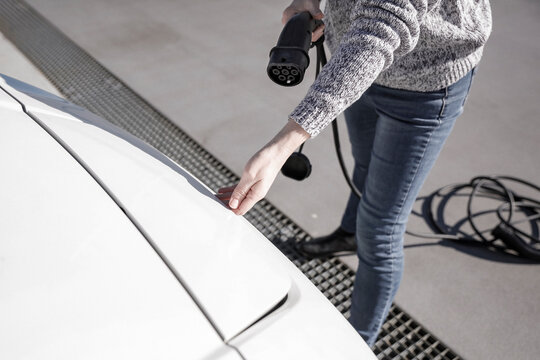 Data Set Training  &ndash; woman charging electric car with EV charging station. Parking area background, providing a realistic everyday environment for electric vehicle charging.