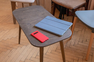 Smartphone and tablet on a wooden table among chairs. Portable devices for communication and digital access. Mobile technology, connectivity and everyday computing. © Анастасия Бурлакова