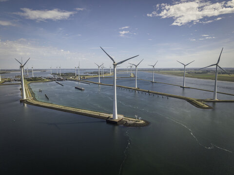 Aerial view of Grevelingendam wind farm with large white wind turbines standing in the water, connected by narrow stone dikes in Bruinisse, Zeeland, Netherlands.