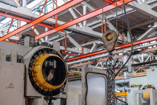 Industrial machinery and heavy-duty chain hoist inside manufacturing plant. Mechanical strength and complex equipment, functional aesthetic of factory floor.