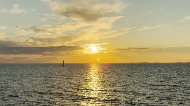 A golden sun sets over open waters as a distant sailboat sails gently. The brilliant reflection creates a calm and peaceful mood across Lake Ladoga.