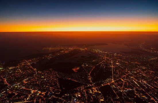 Aerial view of the sprawling cityscape of Karachi at night, with glowing street lights and urban infrastructure illuminated under a vibrant sunset sky in Karachi, Sindh, Pakistan.