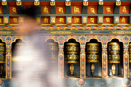 Changangkha Lhakhang, Colorful traditional prayer wheels in ornate temple with blurred figure passing