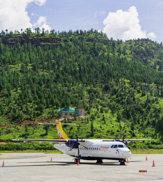 Bhutan Airlines, Paro International Airport, Small white twin-engine propeller airplane parked on tarmac near green hill