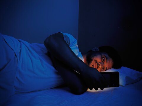 Young asian man using smartphone in dark bedroom at night bed side view stock photo