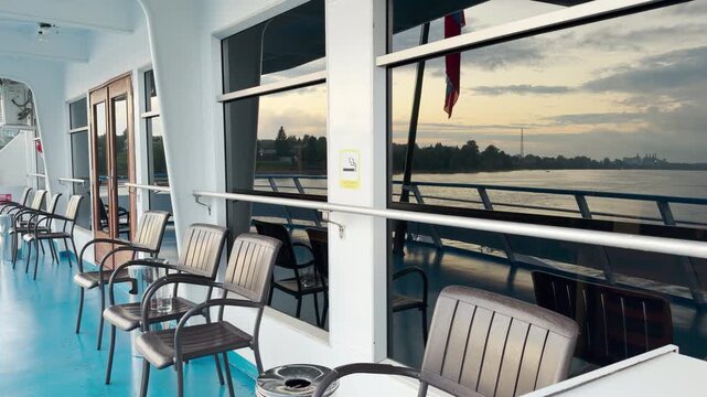 Chairs sit on the cruise ship deck, facing a calm river view. A peaceful and relaxing mood fills the calm evening air during this scenic voyage.