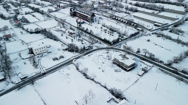 Albania, Boge 11 01 2026: Orbital 4K drone video circling Camping Boga Cabins and Pjeter Ulaj bar, showing snow-covered landscape contrasted by a clear asphalt road.