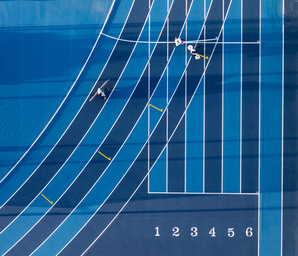 Aerial view of a blue running track with athletes training on the lanes, marked with white lines and numbers in Santo Domingo, Distrito Nacional, Dominican Republic.