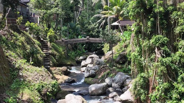 Ancient stone bridge over flowing river at Gunung Kawi temple in Bali, lush tropical jungle scenery, traditional Balinese architecture, serene nature landscape, travel and spiritual destination