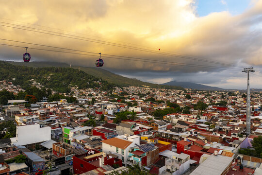 Aerial view of the Teleferico cable car system gliding over dense urban rooftops at sunset with mountains in the background in Uruapan, Michoacan, Mexico.