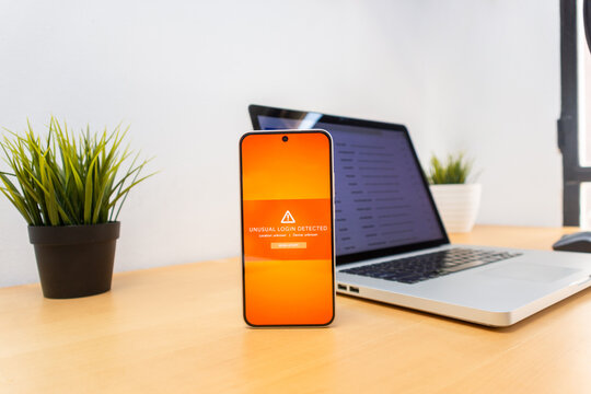 Unusual login warning on smartphone beside laptop with email screen