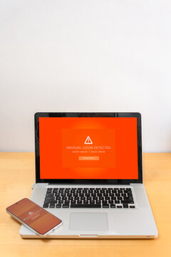 Front view of laptop and smartphone on wooden table displaying unusual login detected alert on screens