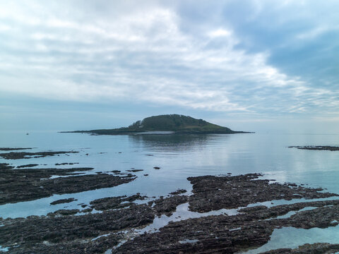 Aerial view of Looe Island surrounded by calm sea and rocky shoreline under a cloudy sky in Looe, Cornwall, United Kingdom.