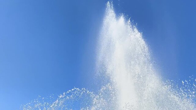 Tall white fountain plume bursts upward against deep blue summer sky