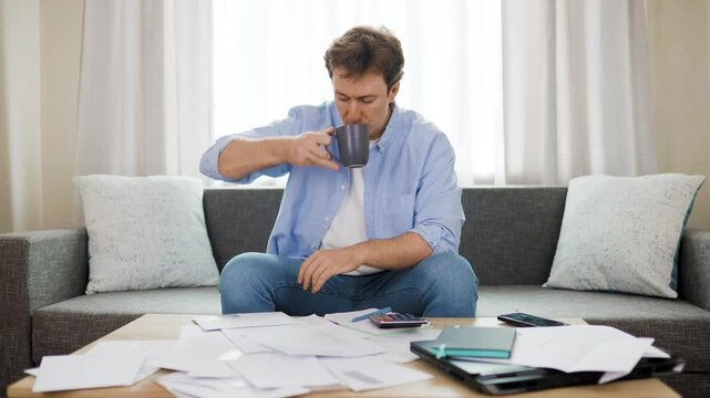 Stressed man opens unpaid utility bills, facing rising energy costs. He drinks coffee and worries about rising household expenses, debt, inflation, and an ongoing financial crisis. 4k footage