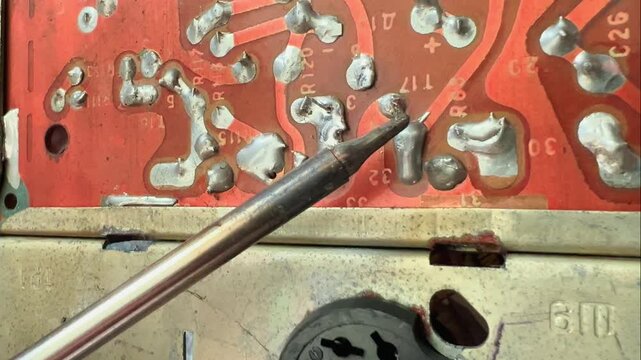Close soldering iron tip heats a contact on vintage electronic circuit board