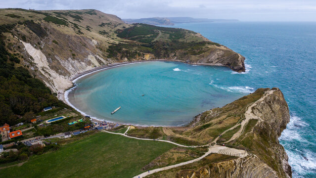 Aerial view of Lulworth Cove featuring a distinctive horseshoe-shaped bay with turquoise water, dramatic limestone cliffs, and grassy headlands along the coast of the United Kingdom.