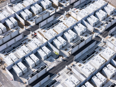 Aerial view of a large-scale battery energy storage system facility with rows of white containers separated by concrete walls and paved access roads in Poland.
