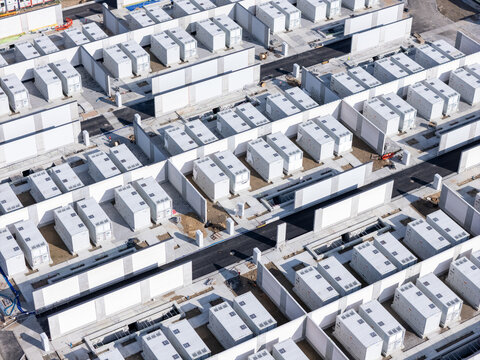 Aerial view of a large-scale battery energy storage system featuring rows of white containerized units separated by concrete walls and paved access paths in Poland.