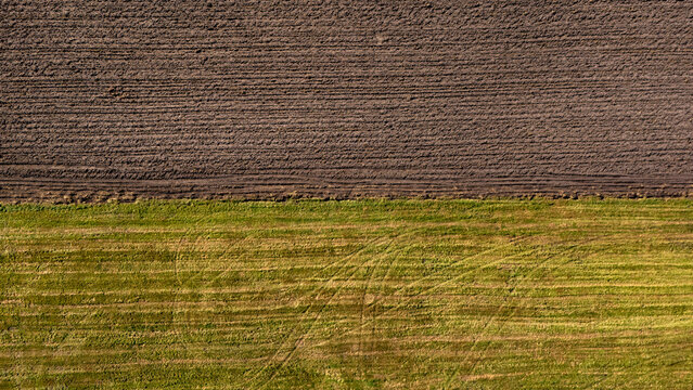 Aerial view of a split agricultural field showing a contrast between dark plowed soil and vibrant green grass in Poland.
