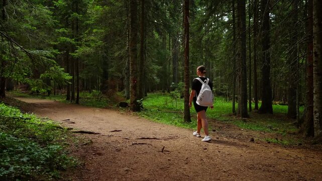 Solo hiker with backpack jogging and walking along tranquil dirt trail through lush green forest, transitioning from active running to relaxed stroll