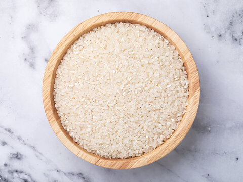 Round grain white rice in wooden bowl on marble table, top view