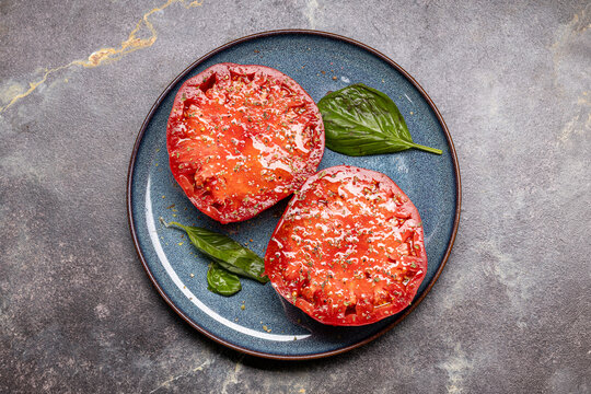 Overhead tomato halves with herbs and basil on a blue plate