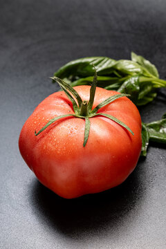 Ribbed tomato with green calyx and water droplets beside basil