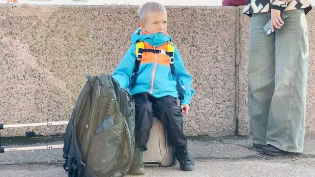 A young boy sits on luggage waiting for a cruise journey. This exciting scene brings happy and curious feelings near the Neva River in Saint Petersburg.
