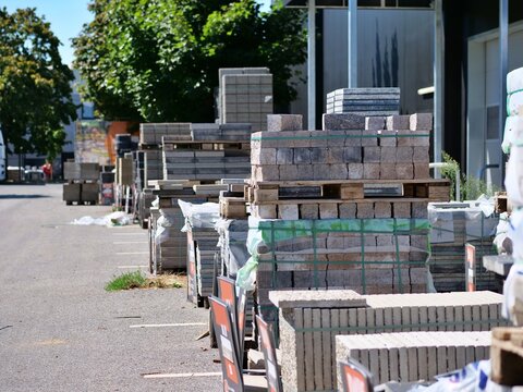 Pallets of stacked concrete paving stones and building bricks stored outside a hardware store supply yard