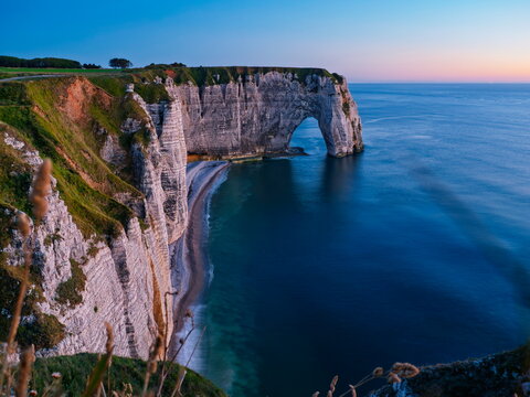 Le Havre, France - 29.06.2015: Dramatic white chalk cliffs and natural stone arch overlooking deep blue ocean at twilight