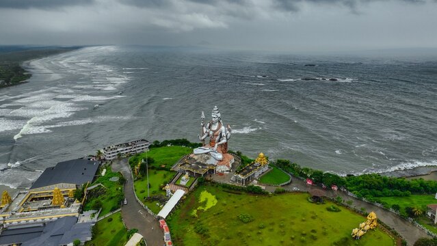 Aerial view of the giant Shiva statue at Murudeshwar Temple overlooking the Arabian Sea with lush green grounds and stormy skies in Murdeshwar, Karnataka, India.