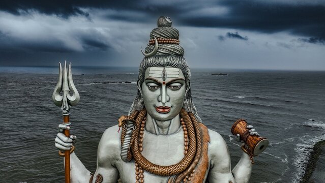 Aerial view of the giant Lord Shiva statue holding a trident and damaru, set against the backdrop of the Arabian Sea under a dramatic cloudy sky in Murdeshwar, Karnataka, India.