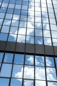 Glass office building facade reflecting blue sky and clouds