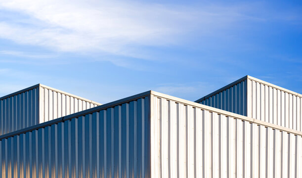 Warehouse industrial factory buildings exterior in modern minimal style with geometric corrugated metal sheet facade and blue sky background