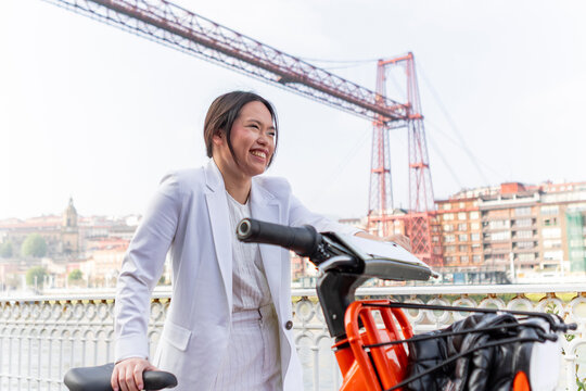 Smiling businesswoman with bicycle near suspension bridge