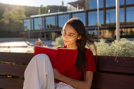 Woman writes in notebook on bench outdoors at sunset