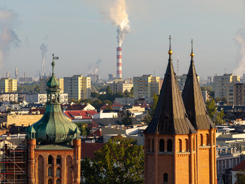 Plock, Poland - 10 September 2026: Aerial view of the historic church towers in the foreground with the industrial chimneys of the ORLEN S.A. refinery visible in the background.