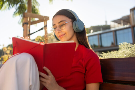 Woman with headphones reading book outdoors in sunlight