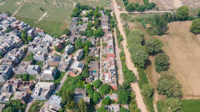 Lahore, Pakistan - 08 September 2026: Aerial view of a residential neighborhood featuring dense housing, flat rooftops, lush green trees, and adjacent agricultural fields.